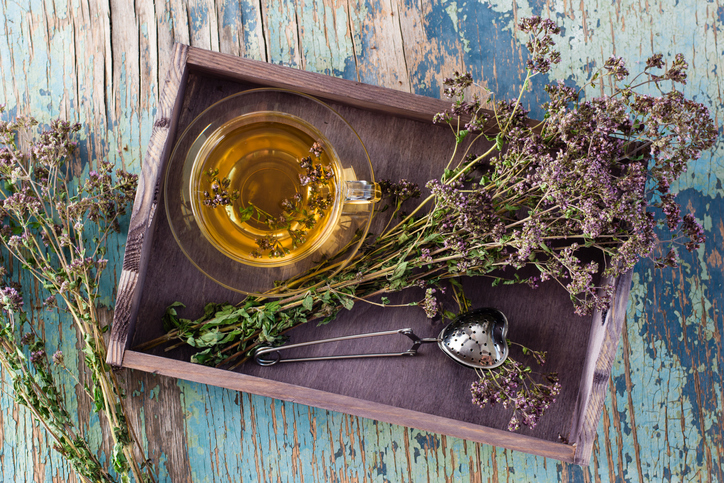 Herbal treatment. Tea with oregano and a bunch of herbs in a wooden tray on the table. Top view